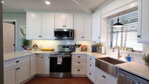 A modern kitchen with white cabinets, stainless steel appliances, and a large window with blinds.