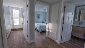 A hallway leading to a bedroom with a bed, a bathroom with a mirror, and a door.