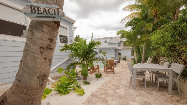A patio area with a wooden table and chairs, surrounded by plants and a sign pointing to the beach.