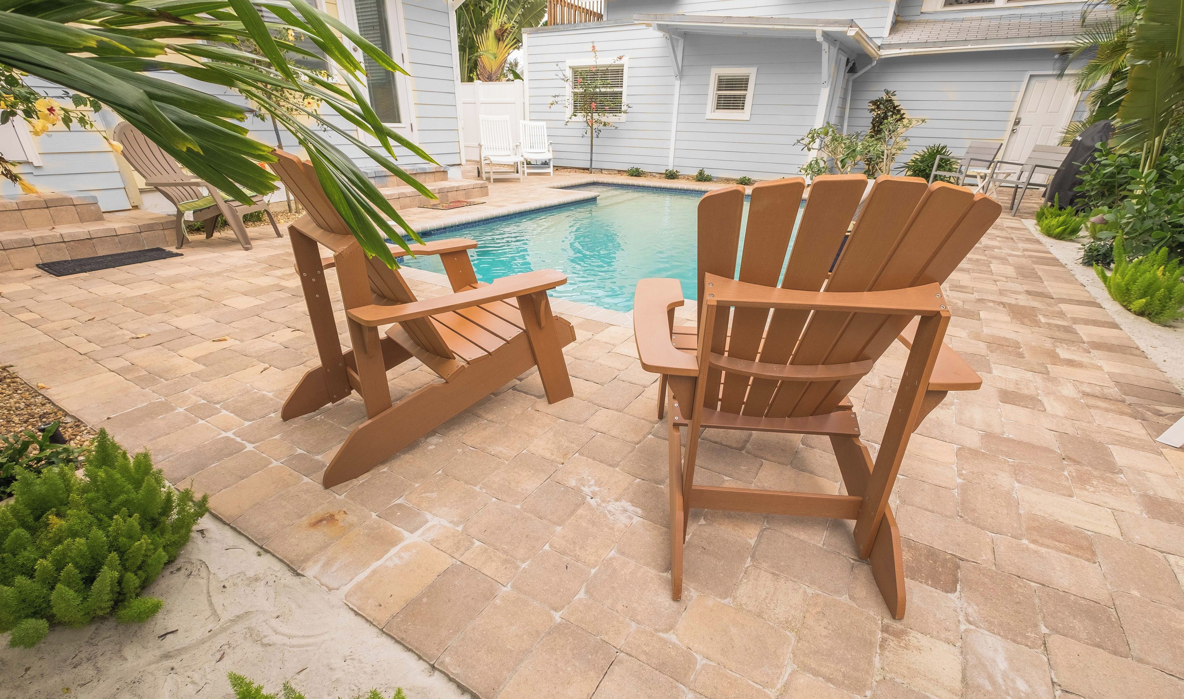 A poolside area with two Adirondack chairs, a small pool, and a house in the background.