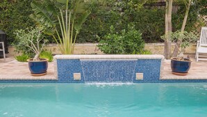A swimming pool with a tiled edge, surrounded by potted plants and a wooden fence.