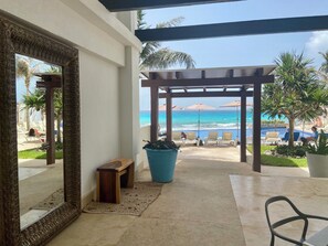 Una habitación con un espejo grande, una banca de madera, una maceta azul y vistas a una playa con sillas y sombrillas reclinables.