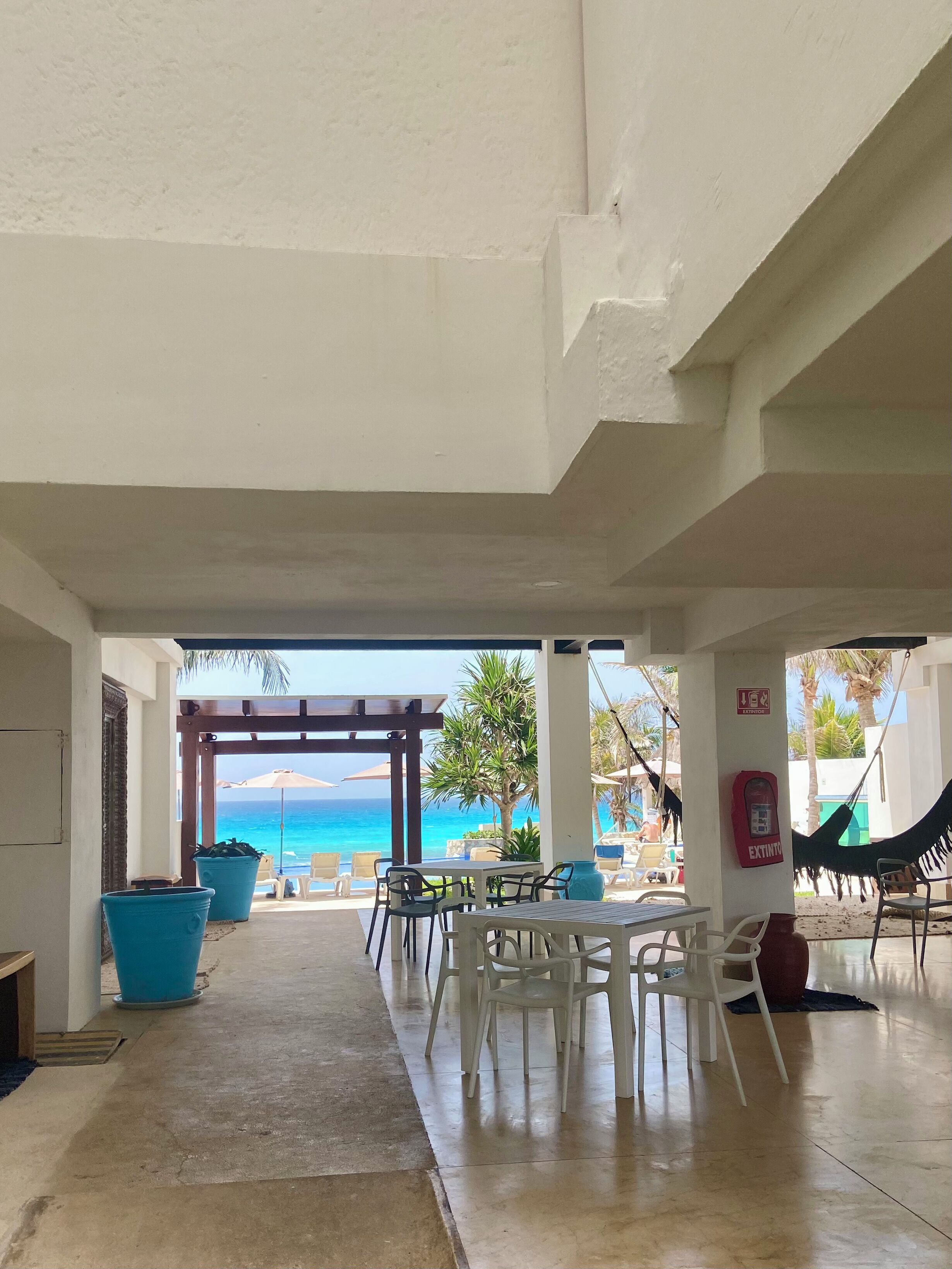 A covered outdoor seating area with tables and chairs, a fire extinguisher, and a view of the ocean.