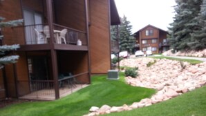 A multi-story building with a balcony, a grassy area, and a rocky slope. - A Canyon's Getaway! 
Perfect for mountain and outdoor lovers (Park City)