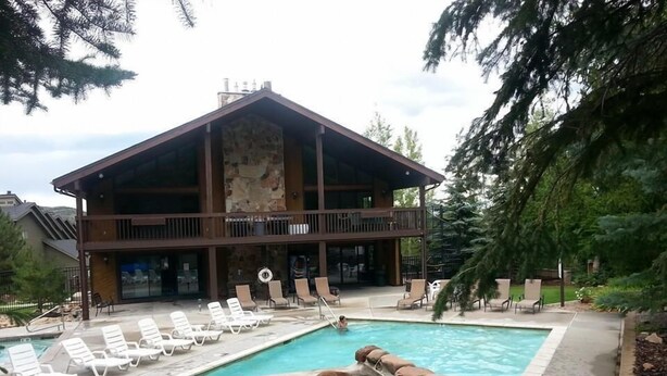 A two-story lodge with a pool area, lounge chairs, and a stone facade. - A Canyon's Getaway! 
Perfect for mountain and outdoor lovers (Park City)