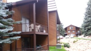 A two-story building with a balcony, a small outdoor seating area, and a well-maintained lawn. - A Canyon's Getaway! 
Perfect for mountain and outdoor lovers (Park City)