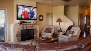 A living room with a fireplace, leather sofa, armchair, and a television mounted on the wall. - Unbelievable Views, Perfect Location, Ski, Golf, Mountain Home (Ruidoso)
