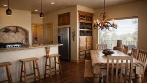 A kitchen with wooden bar stools, a dining table with chairs, a chandelier, and a view of the outdoors. - Unbelievable Views, Perfect Location, Ski, Golf, Mountain Home (Ruidoso)