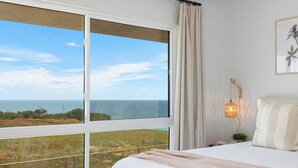 Ein Schlafzimmer mit großem Fenster und Blick auf das Meer und eine grüne Landschaft.