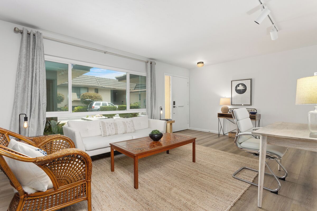A modern living room with a white sofa, wicker chairs, a wooden coffee table, and a dining table with chairs.
