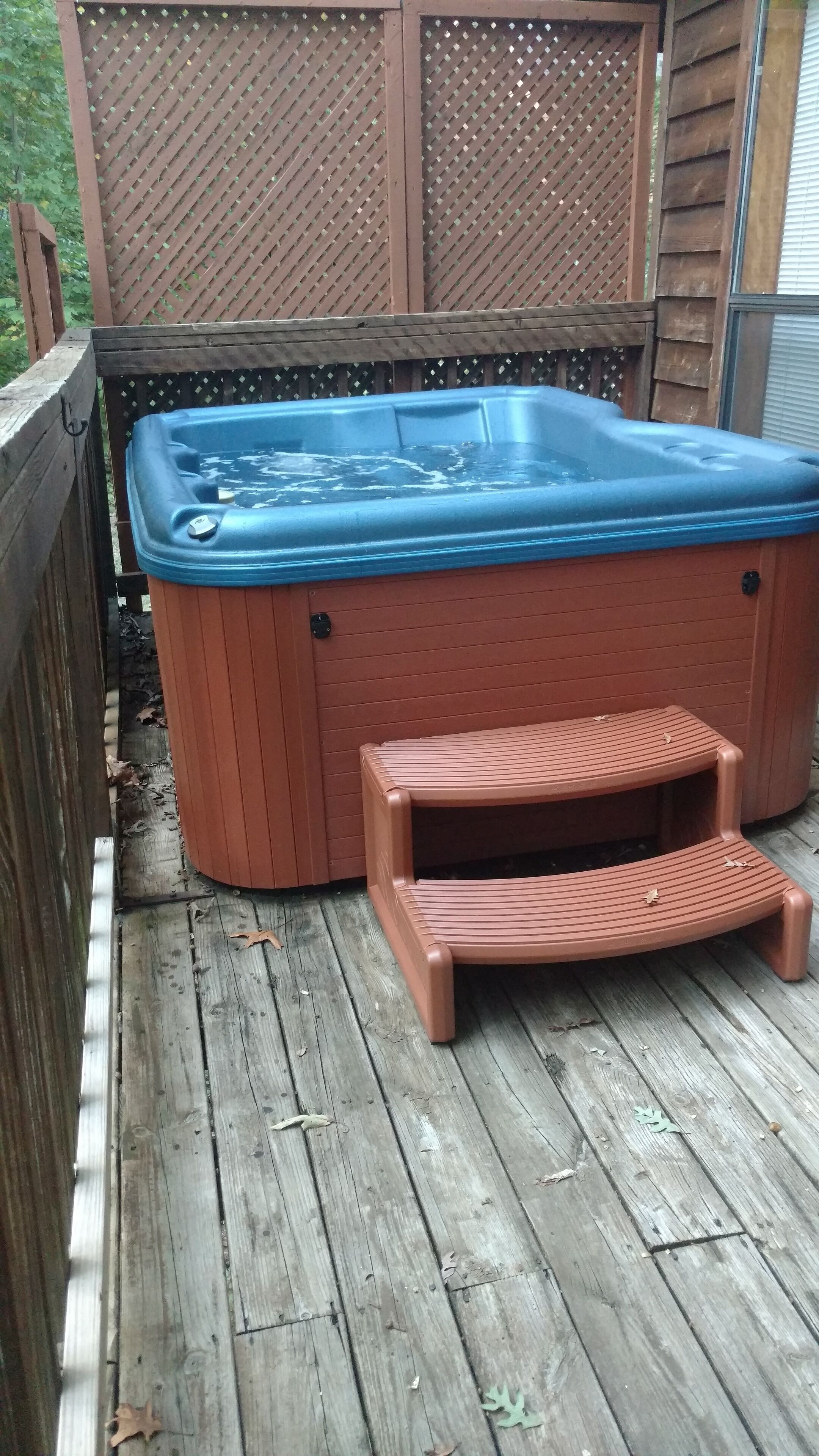 Un jacuzzi en una terraza de madera, con una valla de madera y un panel de celosía al fondo.