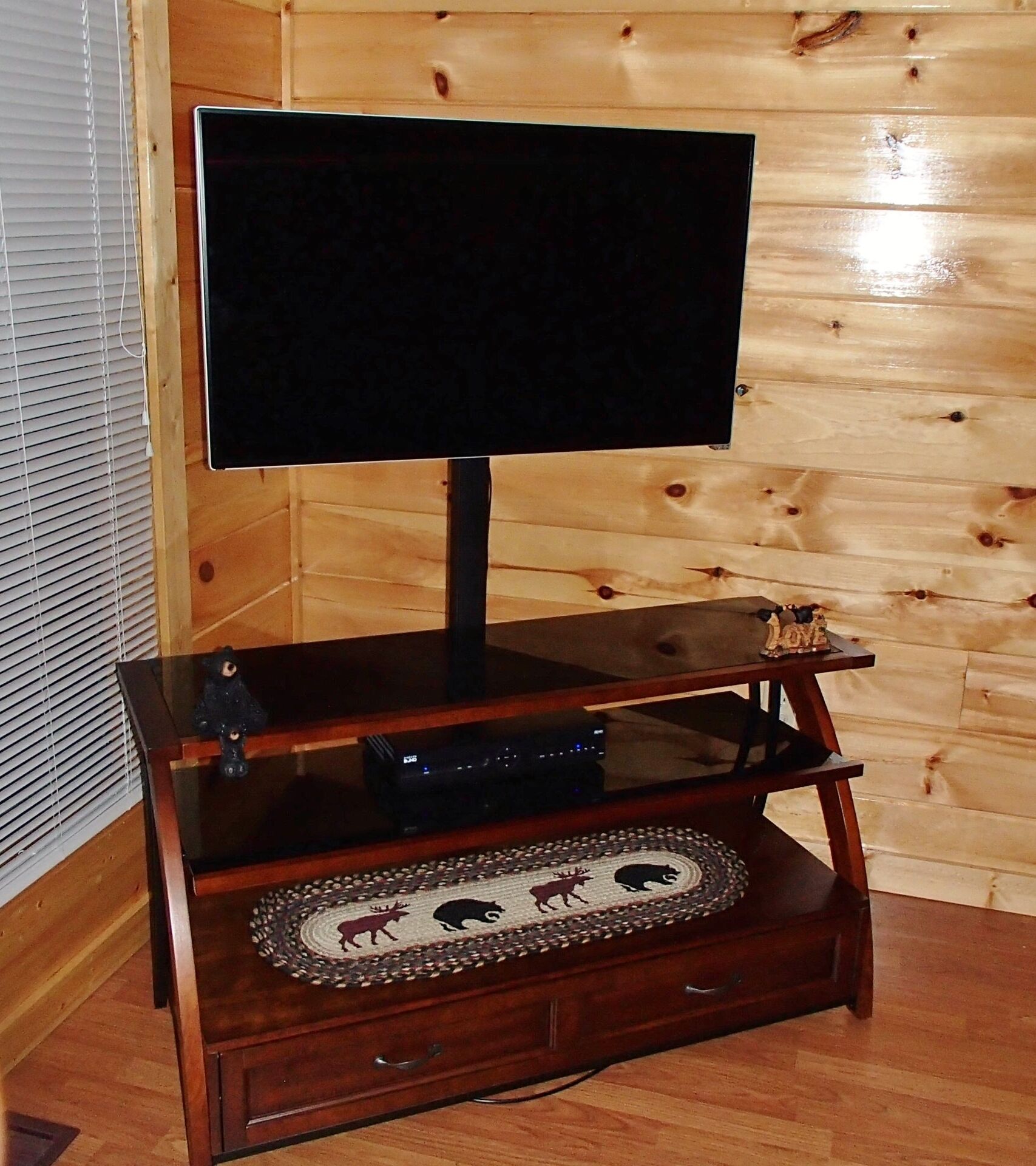Un mueble de entretenimiento de madera con un televisor de pantalla plana, una figura decorativa de un oso y un posavasos tejido con siluetas de animales.