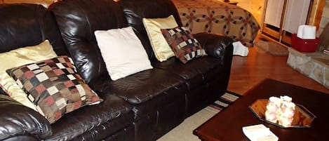 Un salón acogedor con un sofá de cuero, una mesa de centro de madera y una cama con una colcha estampada.