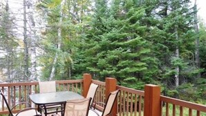 Una terraza de madera con una mesa y sillas, rodeada de un bosque denso.