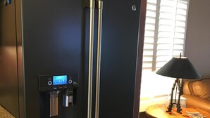 A black refrigerator with a water dispenser and a digital control panel, located in a kitchen with wooden cabinets and a window with blinds. - Pool and Spa (Private) - Tucson Arizona Home (Tucson)