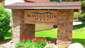 Une enseigne pour le complexe de condominiums Beaver Creek West, avec une arche en pierre et un jardin agrémenté de fleurs rouges et jaunes.
