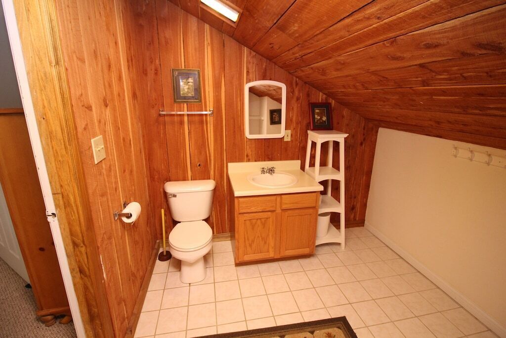 Un baño pequeño con paneles de madera, que incluye inodoro, lavamanos y espejo.