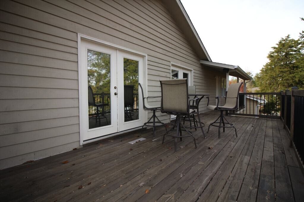 Eine Holzterrasse mit zwei Stühlen und einem Tisch, einer Glasschiebetür und einem kleinen Fenster.