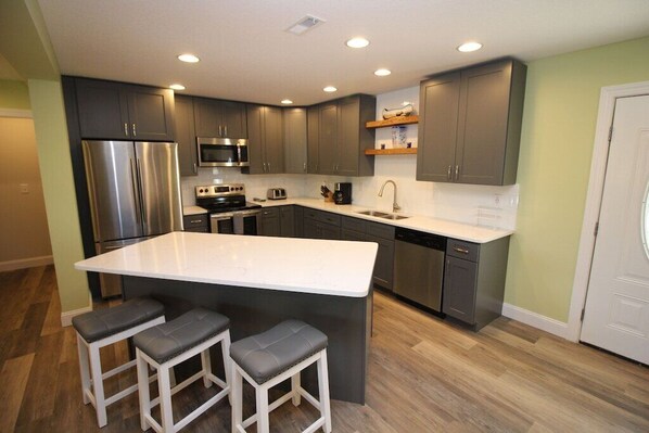 A modern kitchen with a large island, stainless steel appliances, and dark grey cabinets.