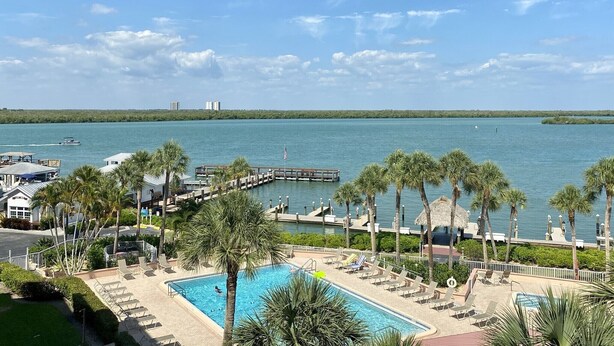A resort with a swimming pool, palm trees, and a view of the water. - Water View of Marco Pass, Heated Pool & Marina-Newly Updated 5th Floor 1Br/1Ba (Marco Island)