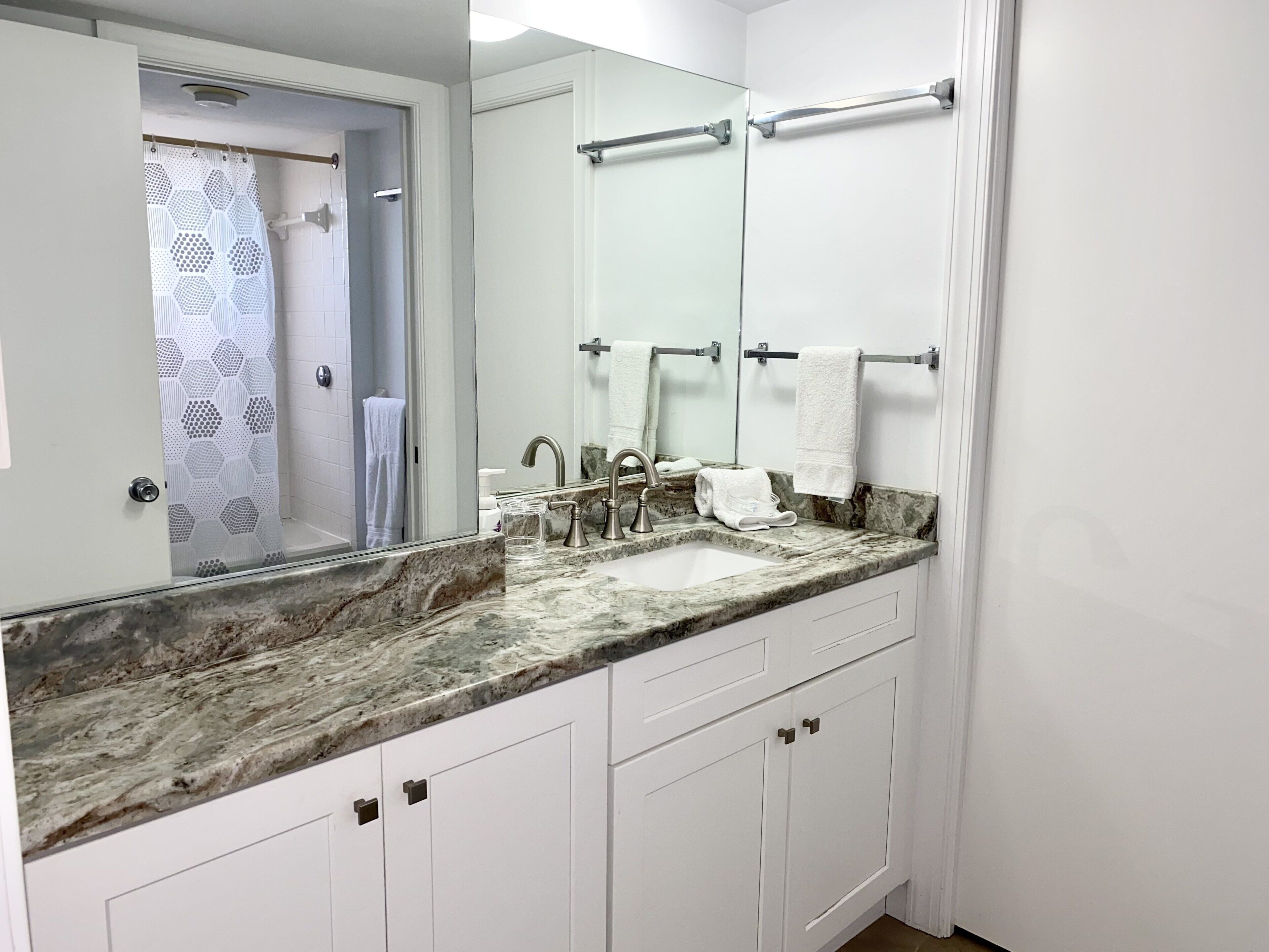 Un bagno con un lavabo in marmo, un grande specchio e mobili bianchi.