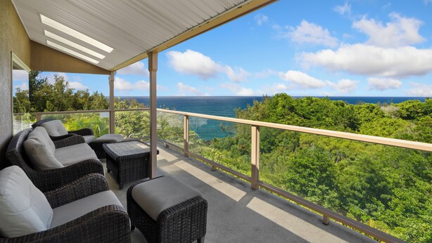 En balkon med fletmøbler og udsigt over et frodigt landskab og havet.