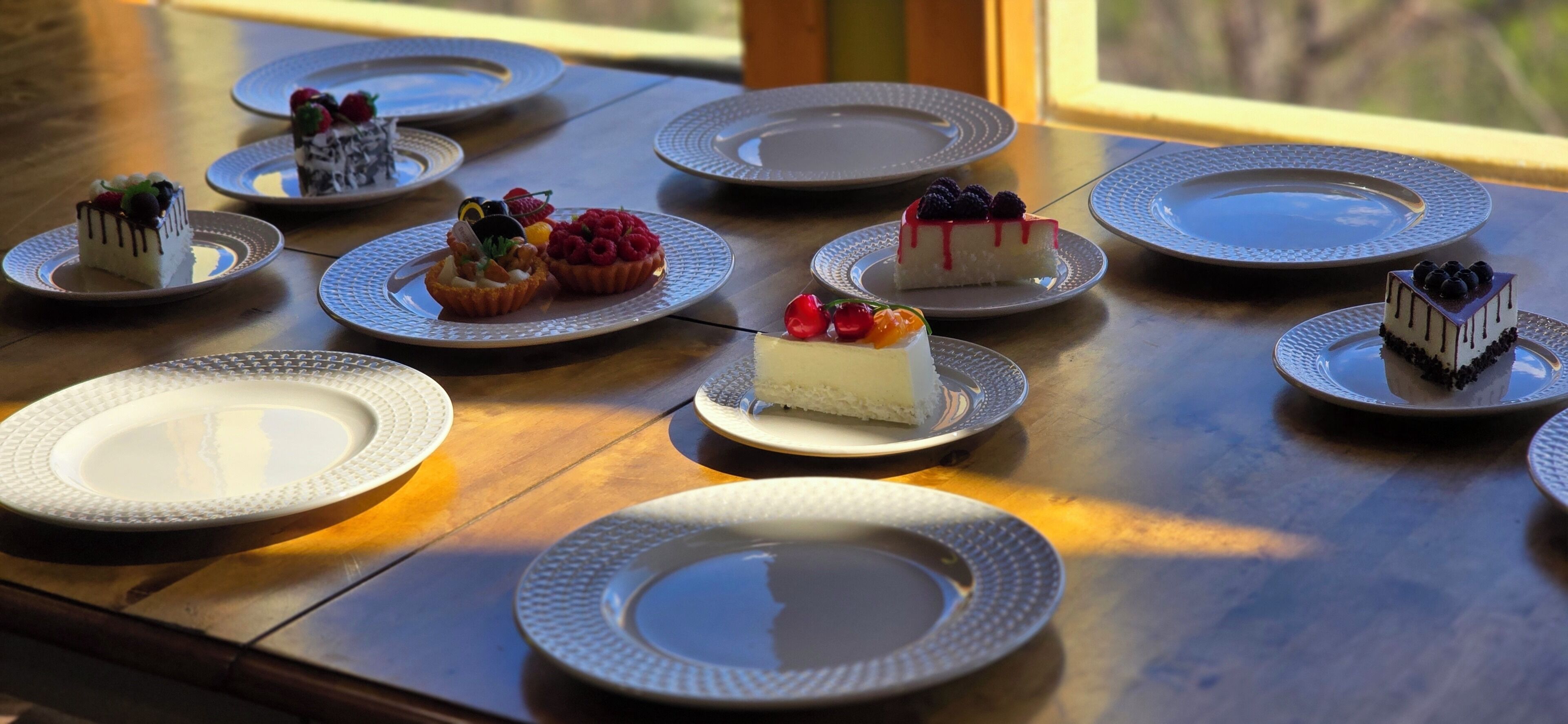 A table with various desserts on plates, arranged on a wooden table with a view outside.