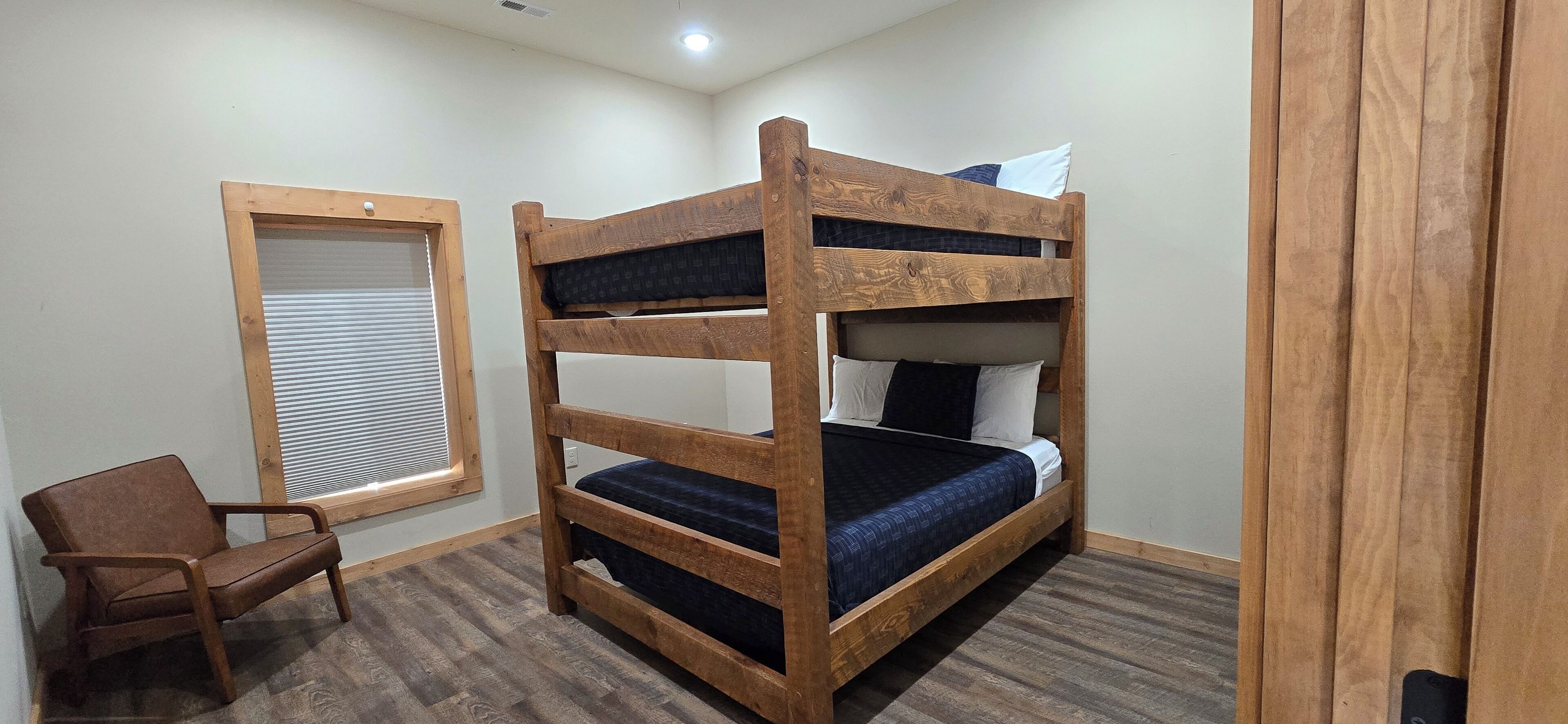 A bunk bed with a wooden frame, a chair, and a window with blinds.