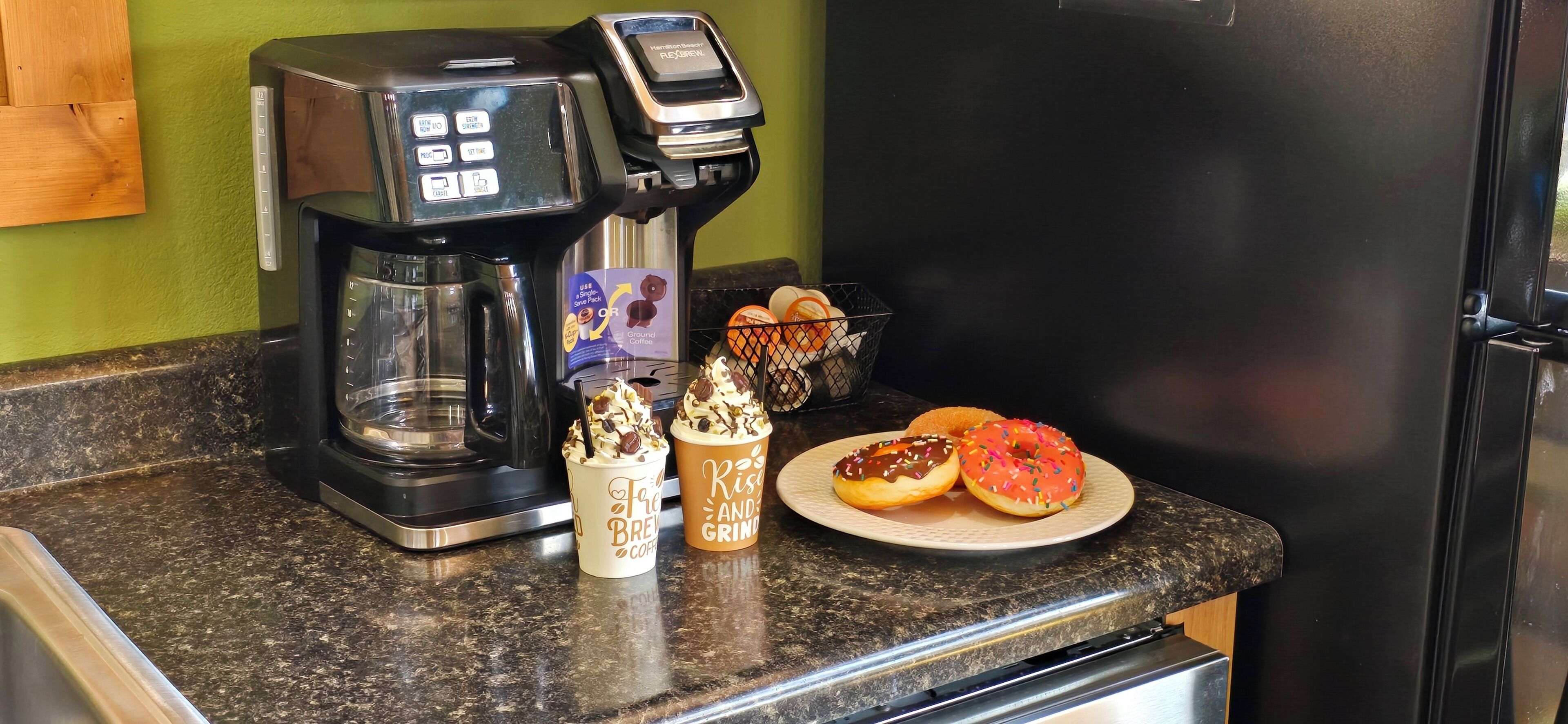 A coffee maker, a plate with donuts, and a coffee cup on a kitchen counter.