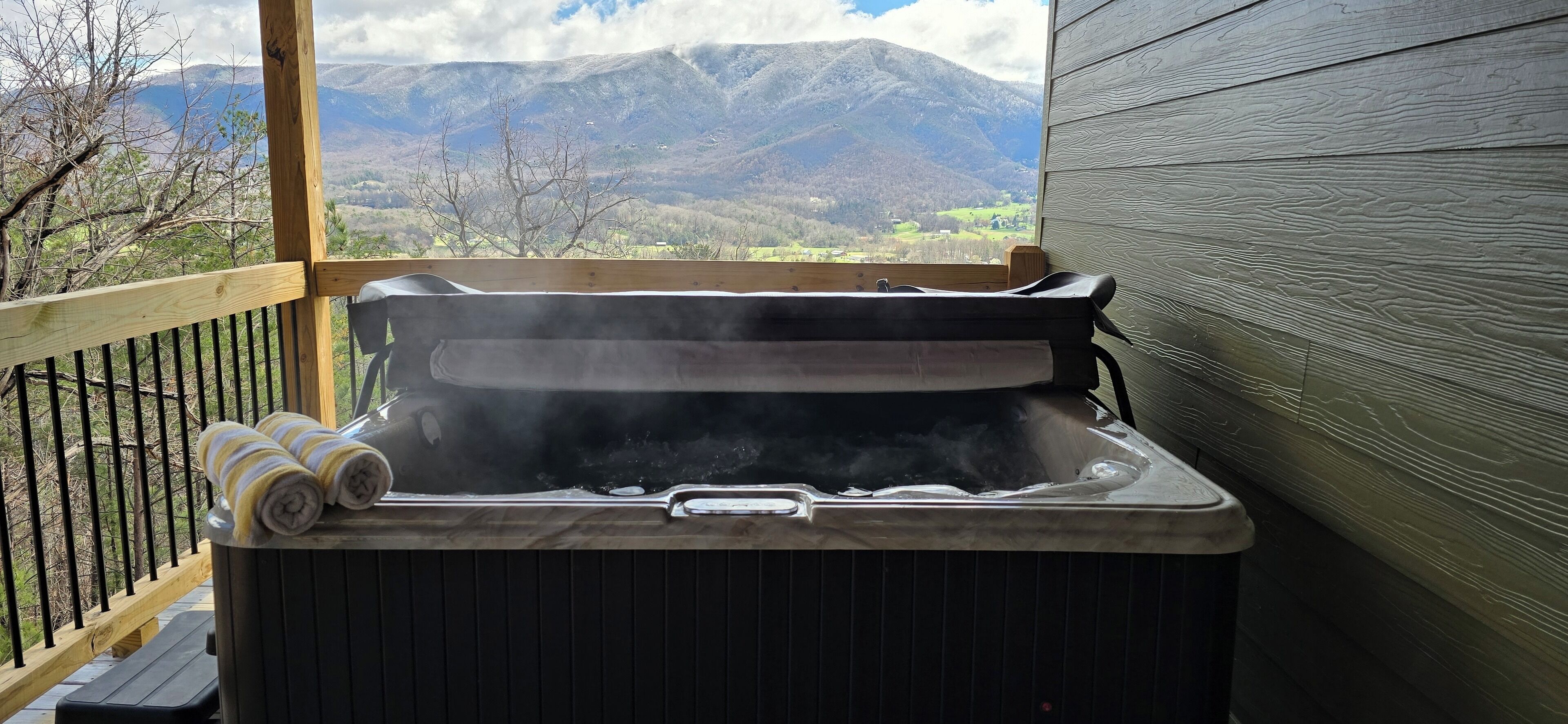 A hot tub on a wooden deck with a mountain view.