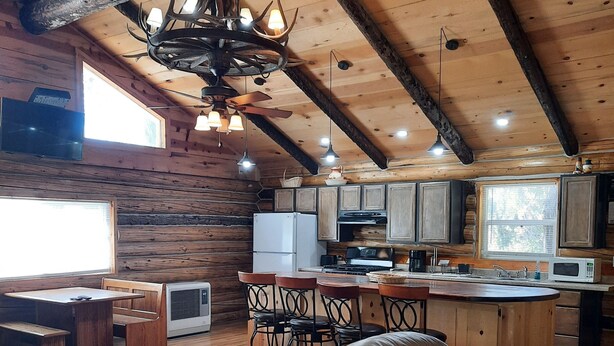 L’intérieur d’un chalet rustique comprend un coin repas, des poutres en bois au plafond et une cuisine équipée d’appareils modernes.