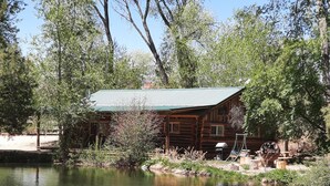 Un chalet rustique au bord d’un lac paisible, entouré d’arbres.