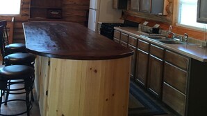 Une cuisine rustique aux murs en bois, avec un îlot central doté de tabourets, une cuisinière et un évier.