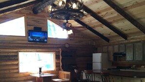 L’intérieur d’une cabane en rondins, avec un canapé, une télévision, une cuisine et des poutres en bois.