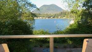 A balcony with a view of a lake and mountains. There are two chairs and a small table.