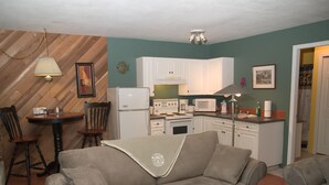 A living room with a sofa, a coffee table, and a dining area with a table and chairs. There is a kitchen area with cabinets, a refrigerator, and a microwave.