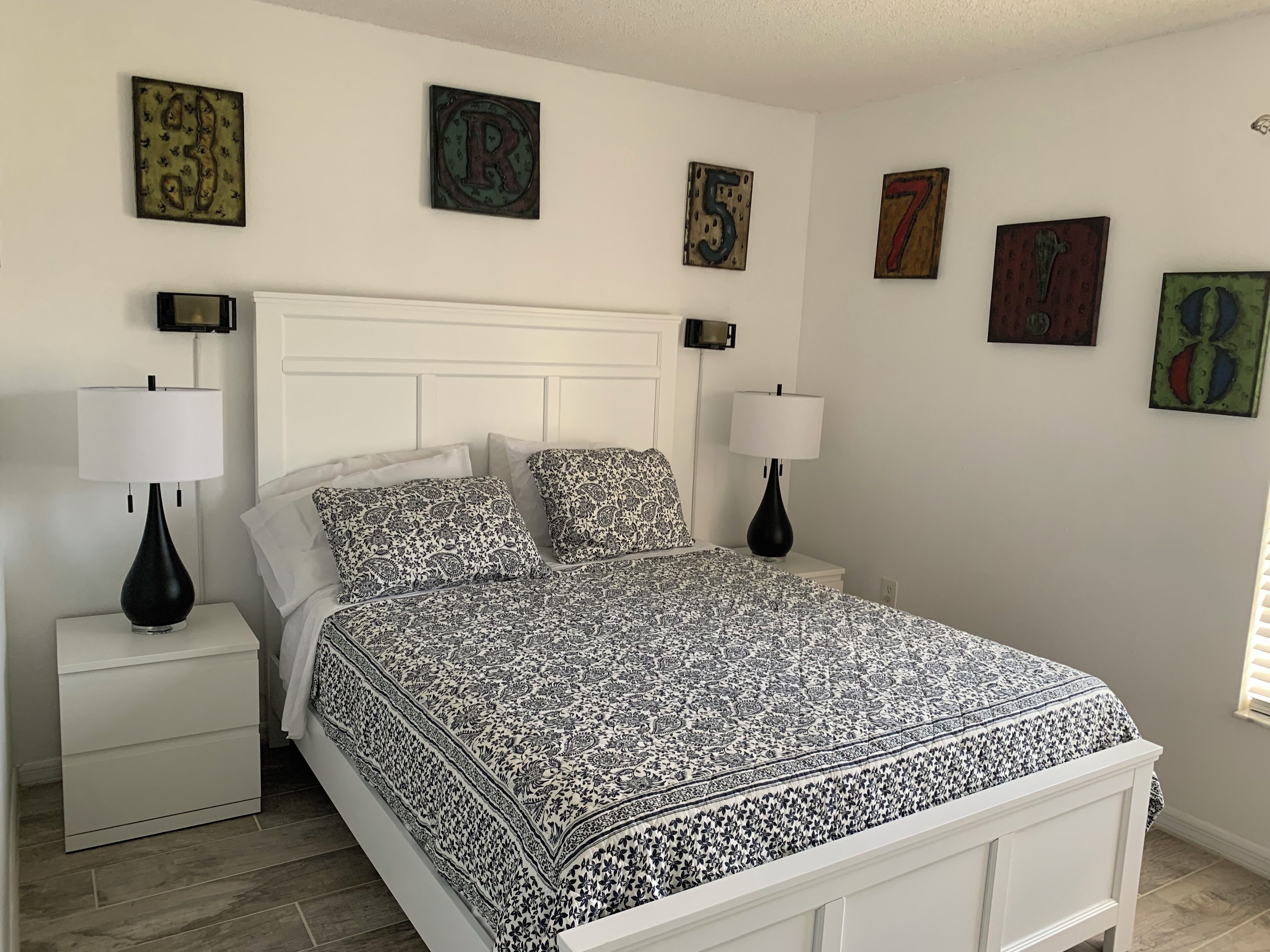 A bedroom with a white bed, patterned bedding, two bedside tables with lamps, and wall art.
