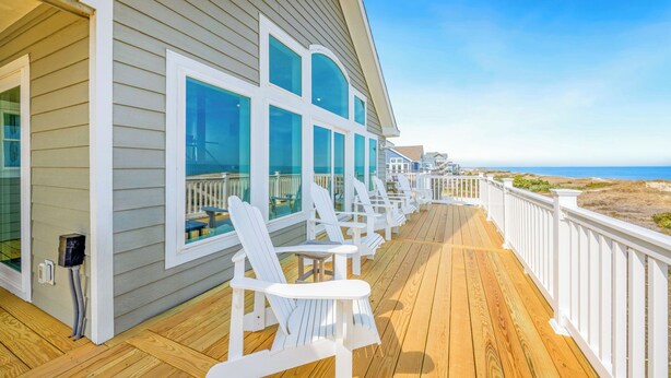 A wooden deck with white chairs and a railing overlooking a beach. - Premier Oceanfront Home in Waves w/ Private Pool, Hot Tub, Game Room, Tiki Bar (Waves)