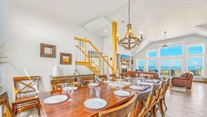 A spacious dining area with a wooden table, chairs, and a staircase leading to an upper level. - Premier Oceanfront Home in Waves w/ Private Pool, Hot Tub, Game Room, Tiki Bar (Waves)