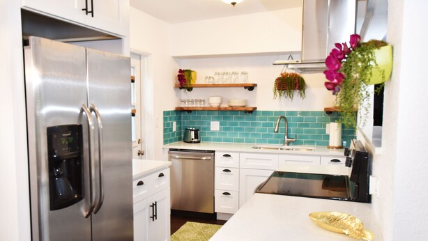 A modern kitchen with a stainless steel refrigerator, white cabinetry, a teal backsplash, and a small island with a gold decorative item. - Corner-Lot 3 Bedroom House, renovated, short walk to the beach! (Cape Canaveral)