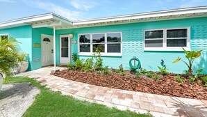 A turquoise building with a white door, a window, and a small garden area with mulch and plants. - Corner-Lot 3 Bedroom House, renovated, short walk to the beach! (Cape Canaveral)