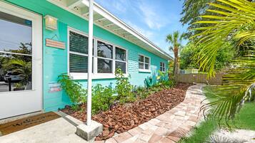 Une maison turquoise avec un jardin bien entretenu, un chemin pavé et une clôture en bois.
