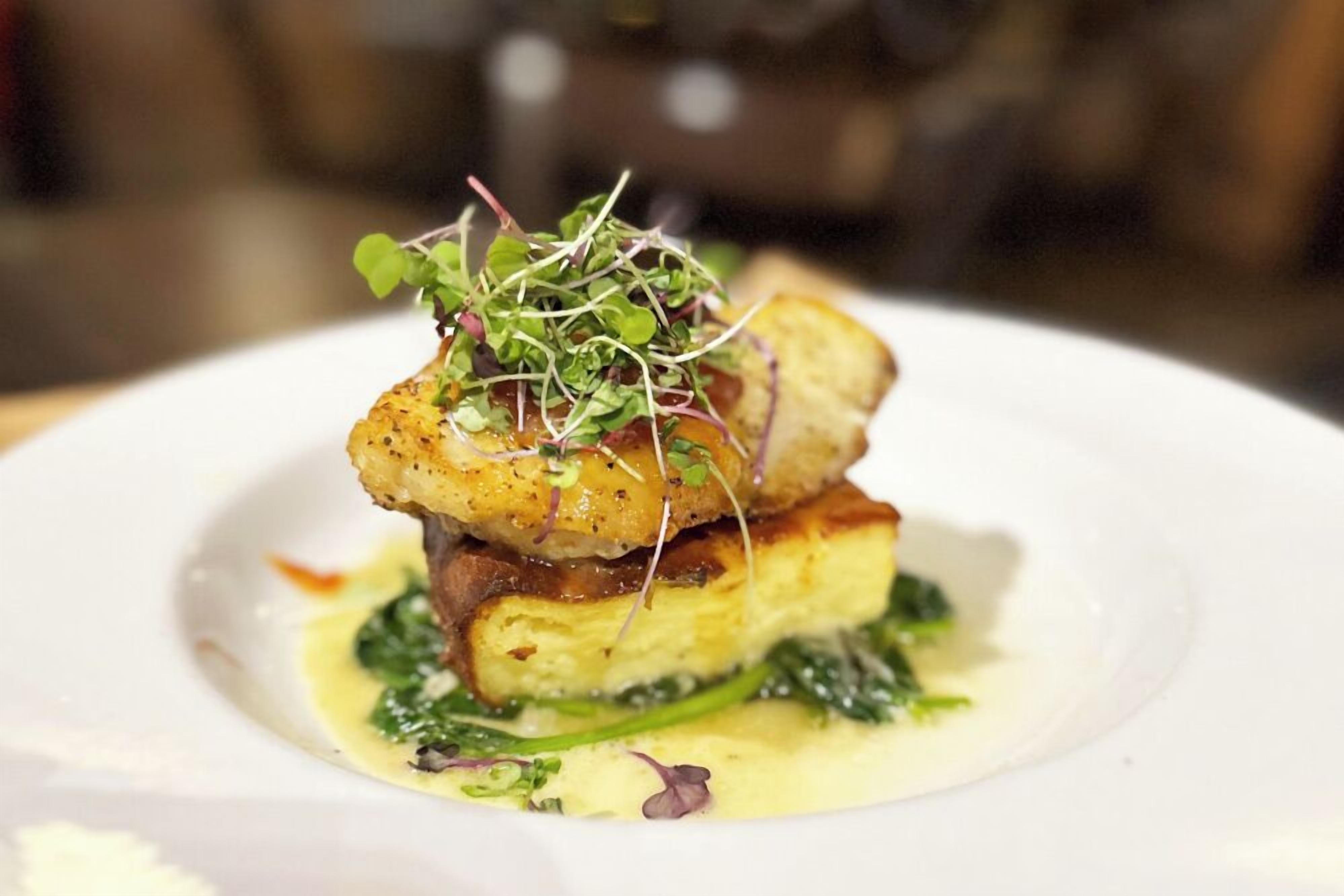A plated dish with a golden-brown crust, greens, and a creamy sauce.