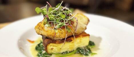 A plated dish with a golden-brown crust, greens, and a creamy sauce.