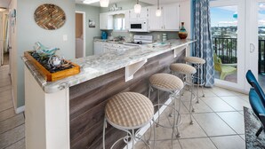 Una cocina moderna con encimera de mármol, armarios blancos y un amplio ventanal con vistas a un balcón.