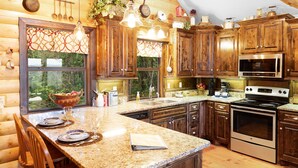 A kitchen with wooden cabinets, granite countertops, a stainless steel oven, and a large window with a view of greenery.