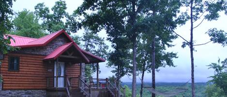 A log cabin with a red roof, wooden porch, and a gravel driveway.