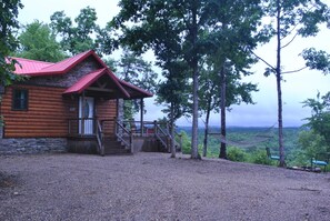 A log cabin with a red roof, wooden porch, and a gravel driveway. - Secluded, luxurious cabin perched above Eagle Fork Creek with sunrise views. (Smithville)