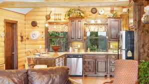 A cozy log cabin interior with a leather sofa, wooden cabinets, and a kitchen area.