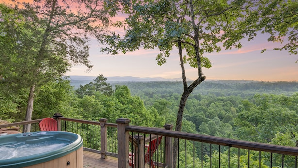 A wooden deck with a hot tub and a red chair, overlooking a forested landscape.